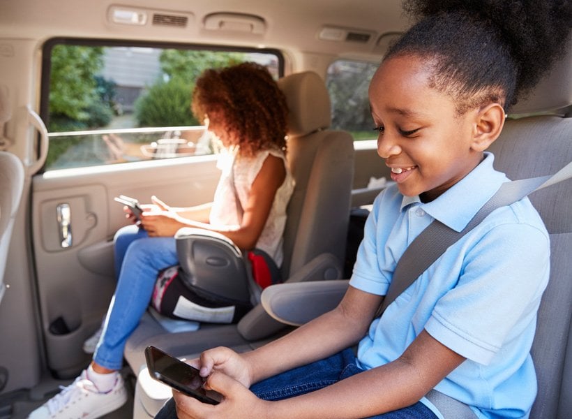 Two children seating in the secind row of a mini van. Each in a booster seat.