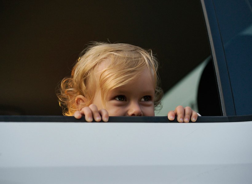 Child in back seat of a car with the window all the way down