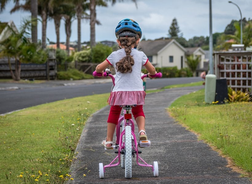 Young girl bicycling on a sidewalk next to a road