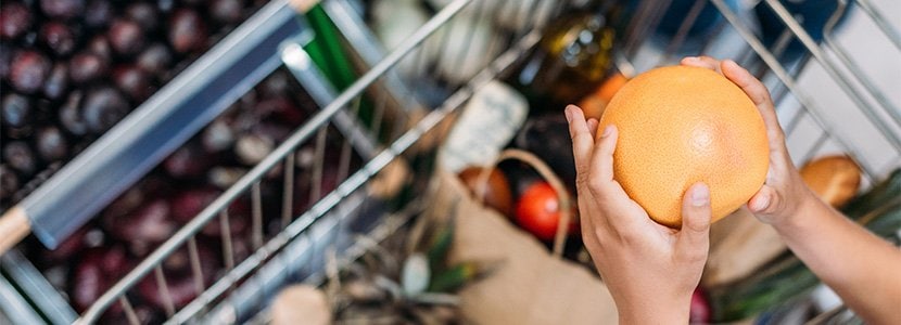 A pair of hands holding a fruit over a shopping cart